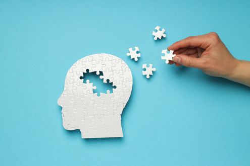 Eine Hand legt ein Puzzle-Teil zu einem weißen Kopf