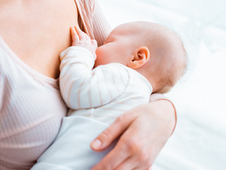 Eine junge Mutter sitzt am Fenster, hält ihr Baby im Arm und stillt