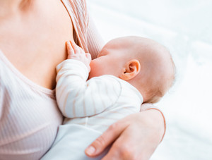 Eine junge Mutter sitzt am Fenster, hält ihr Baby im Arm und stillt