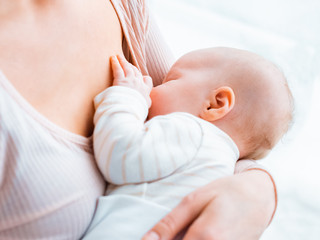 Eine junge Mutter sitzt am Fenster, hält ihr Baby im Arm und stillt