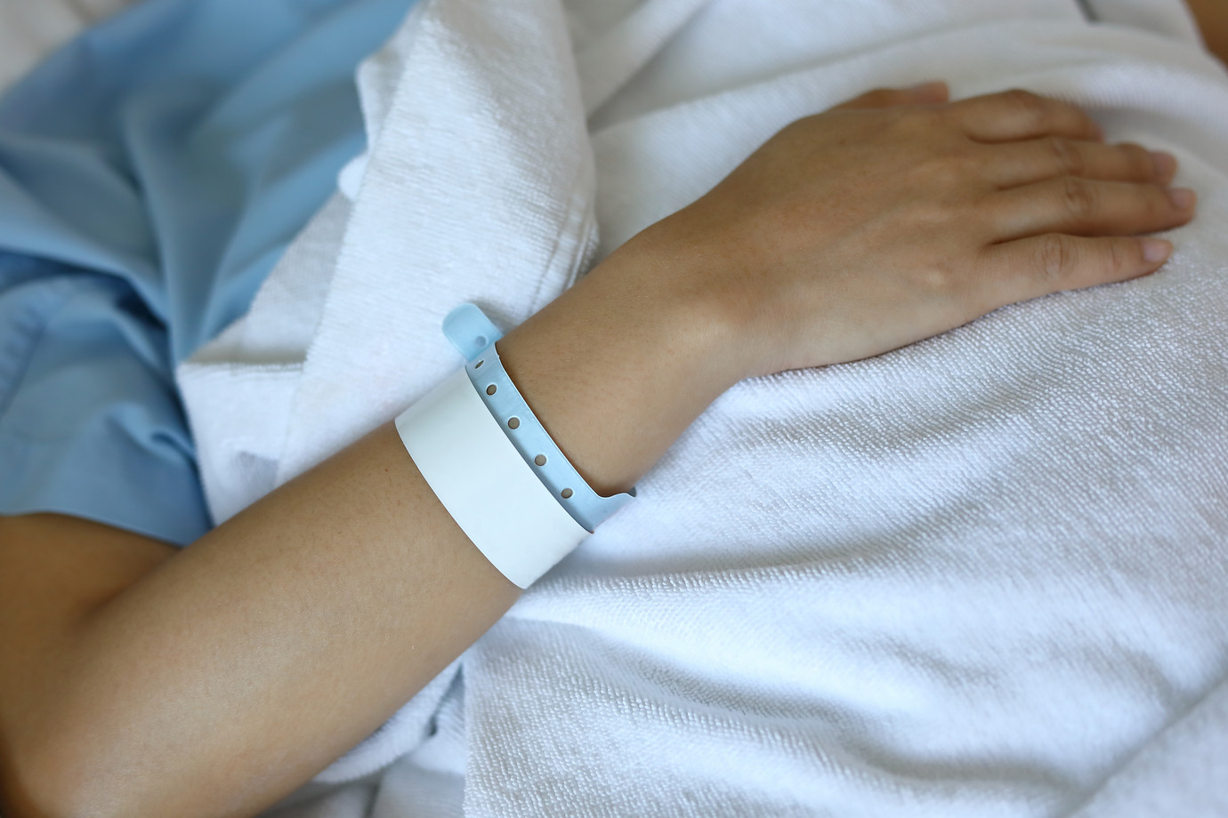 Patient mit weißem Patientenarmband im Bett liegend