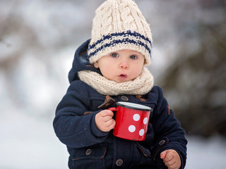 Baby mit Winterkleidung hält eine rote Tasse, im Hintergrund Schnee