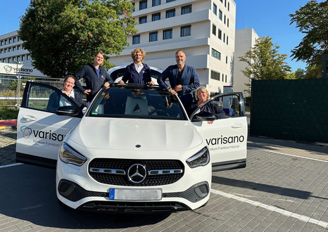 Man sieht ein weißs Auto mit geöffneten Türen auf und um das Auto stehen fünf PErsonen.