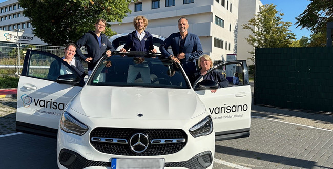 Man sieht ein weißs Auto mit geöffneten Türen auf und um das Auto stehen fünf PErsonen.