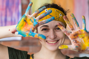 Eine glückliche Frau mit Haarband zeigt ihre bunten Handflächen nach einer Kunsttherapie