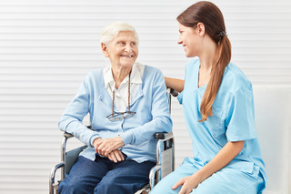 Sitzende ältere Patientin mit Krankenpflegerin die sie umsorgt