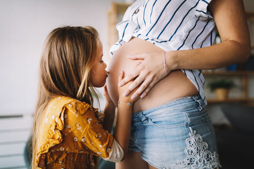 Mädchen küsst Schwangerschaftsbauch der Mutter