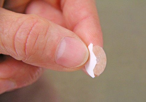 Bildausschnitt zeigt Finger die ein kleines Akupunkturpflaster halten
