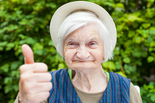 Ältere Seniorin mit Hut zeigt Daumen hoch