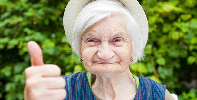 Ältere Seniorin mit Hut zeigt Daumen hoch