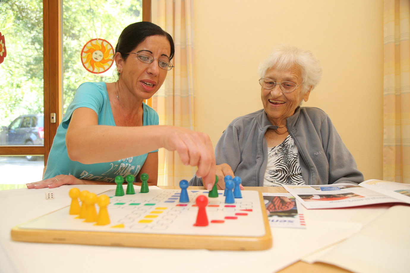 Eine Frau mittleren Alters spielt mit einer älteren Dame ein Brettspiel