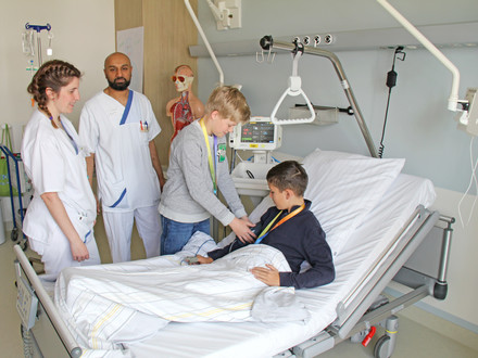 Zwei Praxisanleiter zweigen zwei Jungen wie mal bei Patient:innen die Vitalzeichen misst