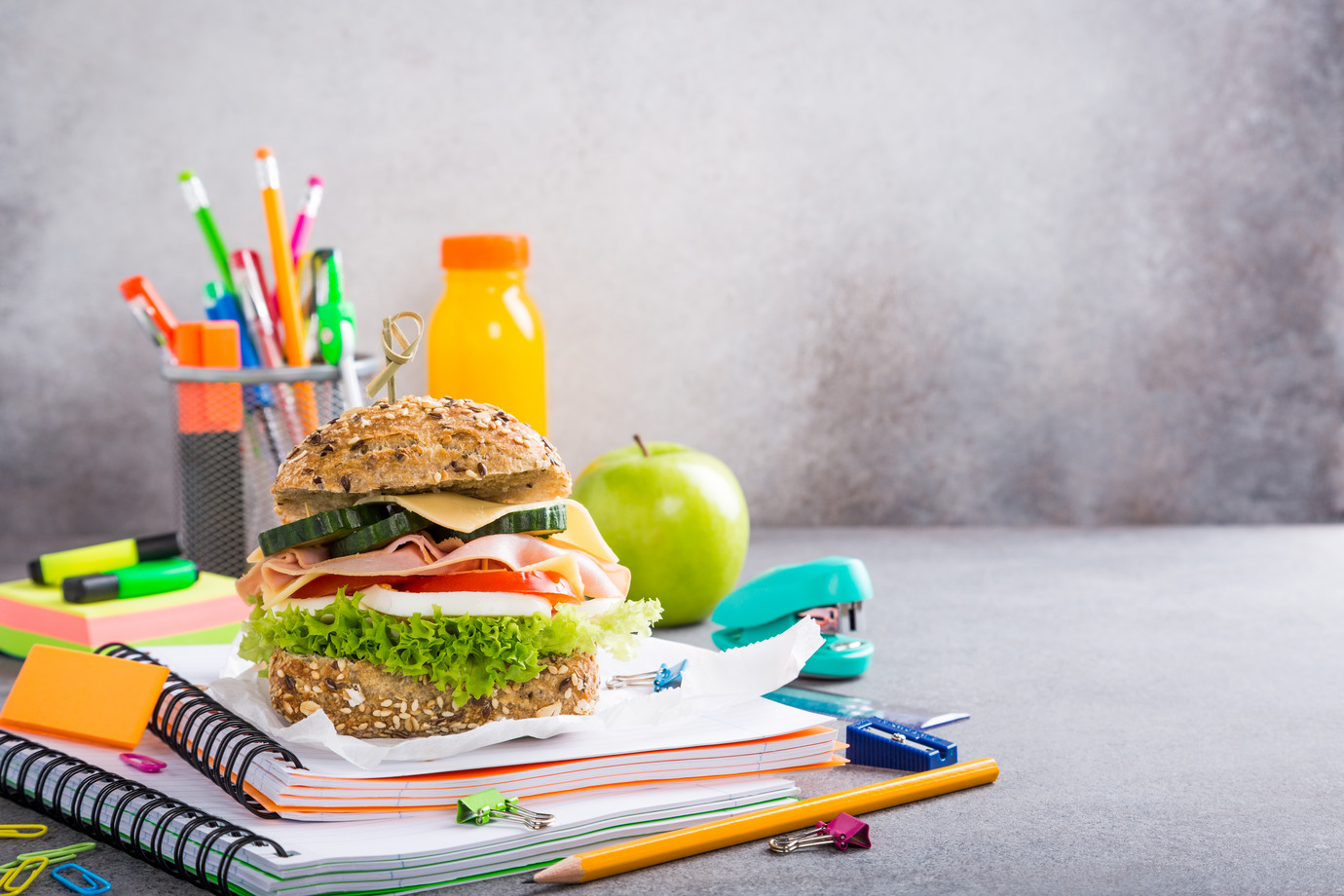 Ein leckerer gesunder Burger liegt auf einem Stapel Schulschreibblöcken, im Hintergrund liegt ein Apfel. 