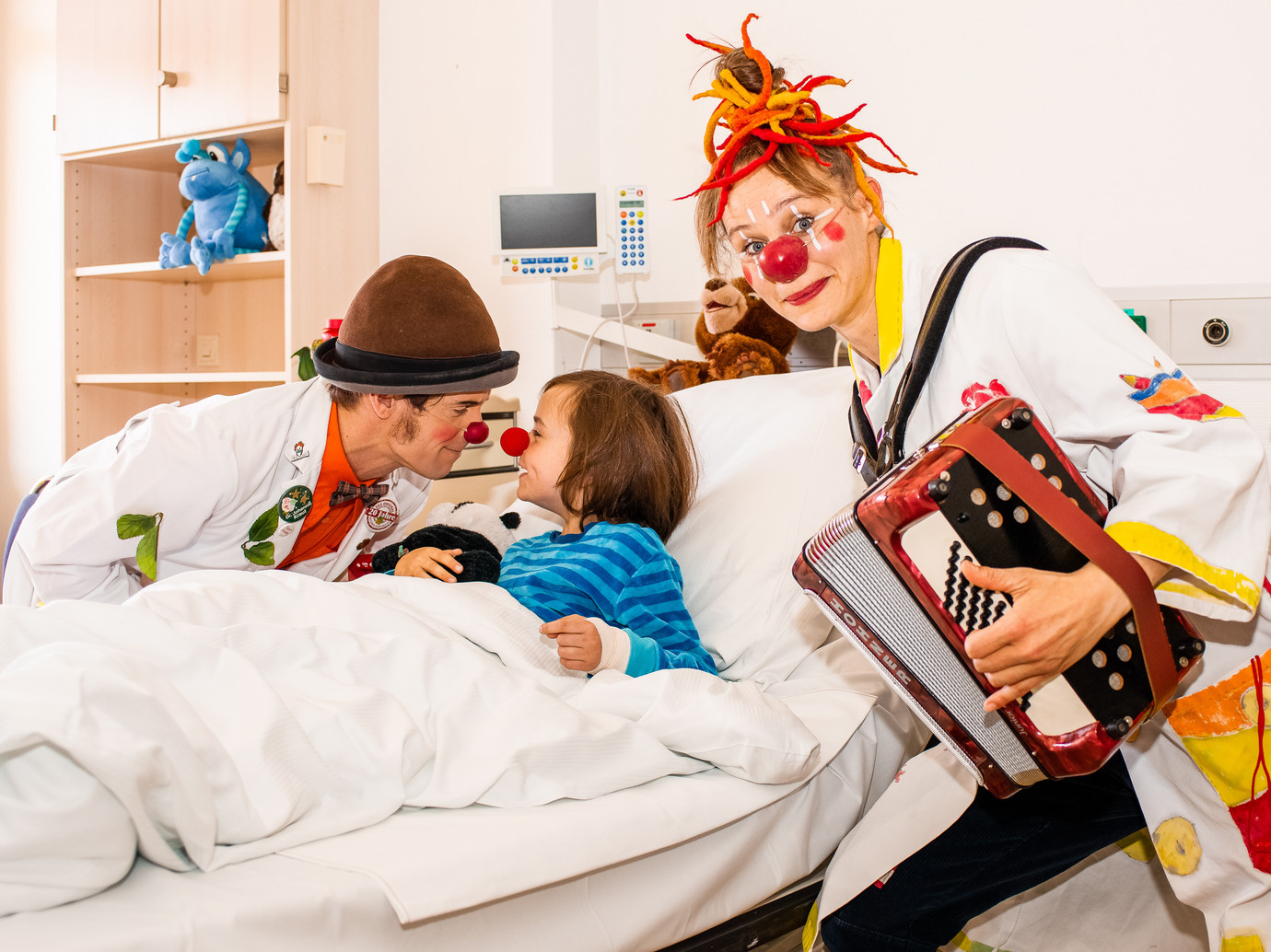 Zwei Clowndoktoren bei einer "Lachvisite" am Bett eines kleinen Patienten