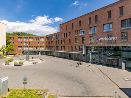 Man sieht einen Platz. AN dessen Ende ein rotes Gebäude, welches das Krankenhaus Bad Soden ist