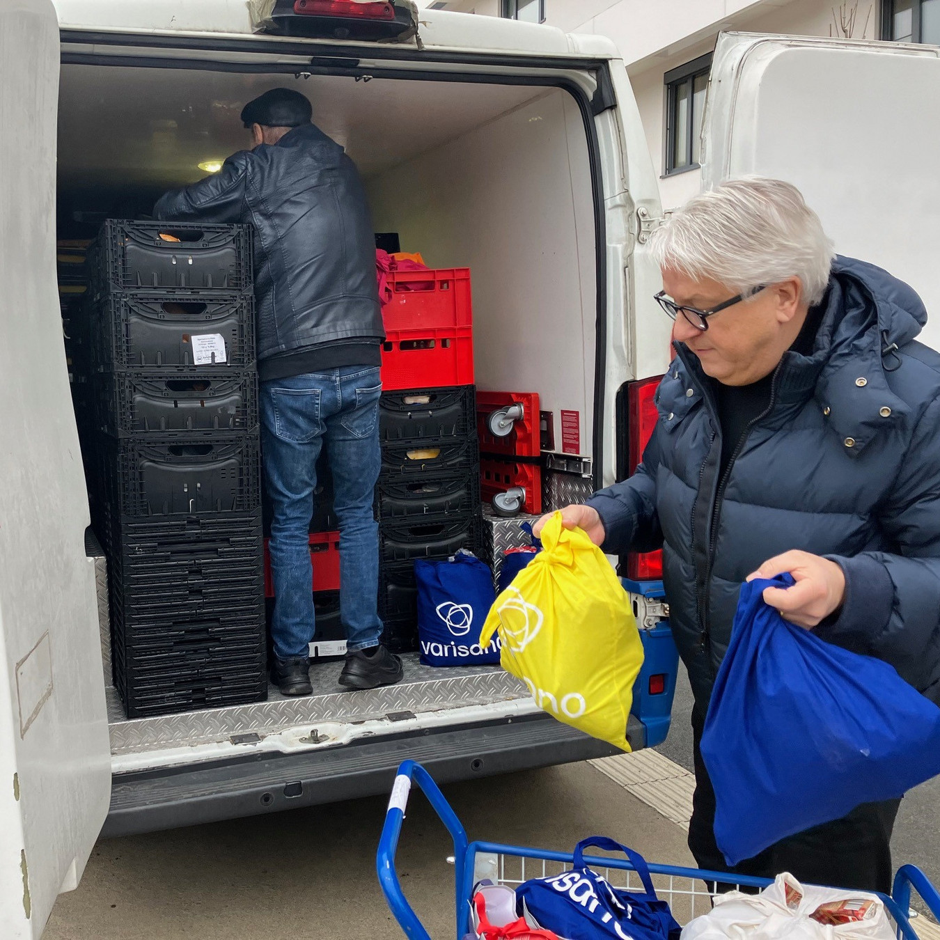 Ein Mann- Geschäfsführer Michael Osypka - hilft einem anderen Mann einen Transporter mit Taschen von varisano zu beladen.